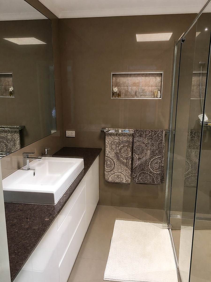 Dark-tiled bathroom with glass shower and white vanity.